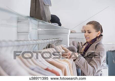 Stock Photography - Side view of young woman choosing sweater in store. Fotosearch