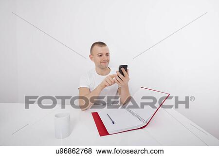 Smiling businessman text messaging on cell phone at desk View Large Photo Image Stock Photo - Smiling businessman text messaging on cell phone at desk. Fotosearch