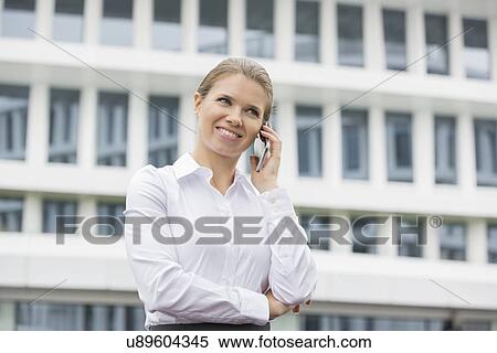 Stock Photography - Smiling businesswoman using cell phone outside office. Fotosearch