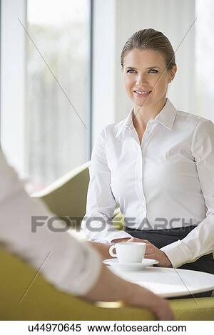 Stock Photography - Smiling businesswoman with colleague at office lobby. Fotosearch