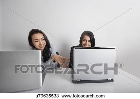 Stock Image - Smiling businesswomen using laptop at desk in office. Fotosearch