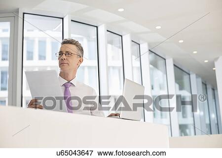 Thoughtful businessman with laptop and documents at railing View Large Photo Image Stock Photo - Thoughtful businessman with laptop and documents at railing. Fotosearch