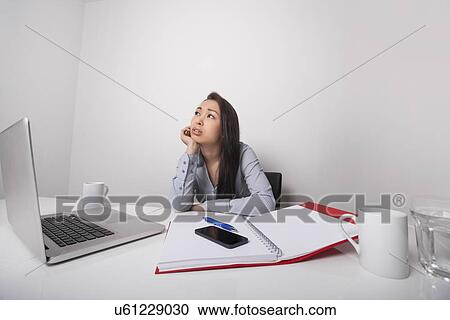 Stock Image - Thoughtful businesswoman sitting at desk in office. Fotosearch