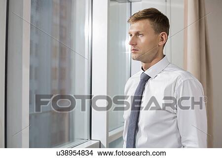 Picture - Thoughtful mid adult businessman looking through window at home. Fotosearch