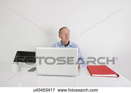 Thoughtful senior businessman using laptop at office desk View Large Photo Image Stock Photo - Thoughtful senior businessman using laptop at office desk. Fotosearch