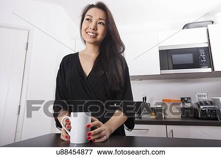 Thoughtful young woman having coffee in kitchen View Large Photo Image Stock Photo - Thoughtful young woman having coffee in kitchen. Fotosearch