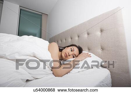 Thoughtful young woman lying in bed View Large Photo Image Stock Photo - Thoughtful young woman lying in bed. Fotosearch