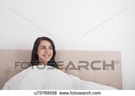 Thoughtful young woman smiling in bed View Large Photo Image Stock Photo - Thoughtful young woman smiling in bed. Fotosearch
