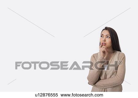 Stock Photography - Thoughtful young woman standing against gray background. Fotosearch