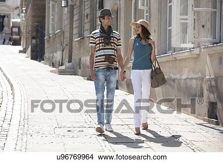 Tourist couple holding hands while walking on sidewalk View Large Photo Image Picture - Tourist couple holding hands while walking on sidewalk. Fotosearch