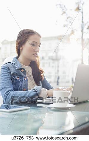 Stock Image - Woman using laptop at sidewalk cafe. Fotosearch