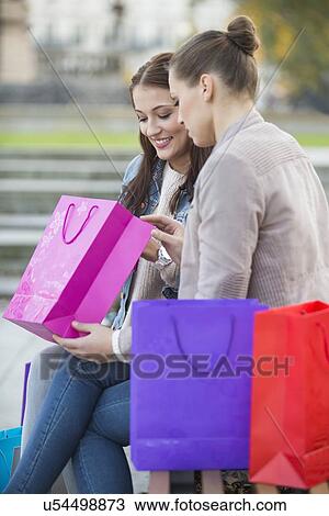Stock Image - Woman with friend looking into shopping bag outdoors. Fotosearch