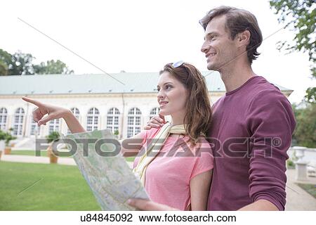 Stock Image - Woman with map showing something to man against building. Fotosearch
