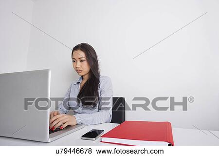 Stock Photo - Young businesswoman using laptop at office desk. Fotosearch