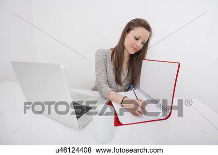 Young businesswoman writing in book at office desk View Large Photo Image Stock Photo - Young businesswoman writing in book at office desk. Fotosearch