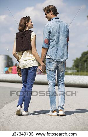 Stock Image - Young couple looking at each other while holding hands on street. Fotosearch