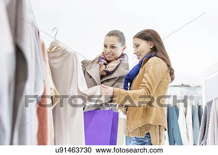 Stock Image - Young female friends choosing sweater in store. Fotosearch