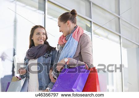Stock Photo - Young female friends looking at each other against store. Fotosearch