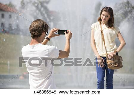 Stock Photography - Young man photographing woman against fountain. Fotosearch