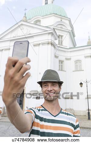 Stock Photo - Young man taking self portrait outside St. Casimir Church, Warsaw, Poland. Fotosearch