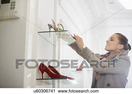 Stock Image - Young woman admiring footwear in store. Fotosearch