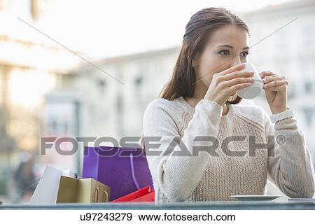 Young woman drinking coffee at sidewalk cafe View Large Photo Image Stock Photo - Young woman drinking coffee at sidewalk cafe. Fotosearch