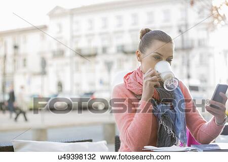 Young woman drinking coffee while using cell phone at sidewalk cafe View Large Photo Image Stock Image - Young woman drinking coffee while using cell phone at sidewalk cafe. Fotosearch