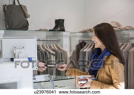 Stock Image - Young woman giving credit card to cashier. Fotosearch