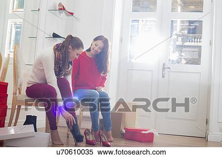 Stock Photography - Young woman looking at friend trying on footwear in store. Fotosearch