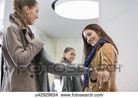 Young woman looking at friend wearing jacket in clothing store View Large Photo Image Picture - Young woman looking at friend wearing jacket in clothing store. Fotosearch