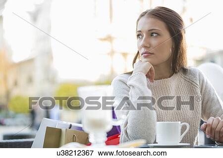 Young woman looking away while sitting at sidewalk cafe View Large Photo Image Stock Photo - Young woman looking away while sitting at sidewalk cafe. Fotosearch
