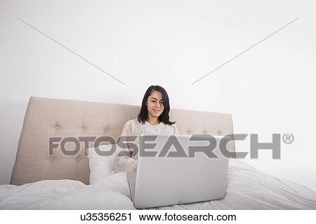 Young woman using laptop on bed View Large Photo Image Stock Image - Young woman using laptop on bed. Fotosearch