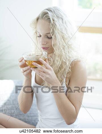 Stock Image - Young woman with eyes closed enjoying herbal tea in house. Fotosearch