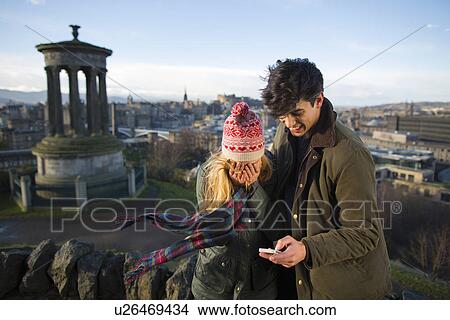 Picture - A young couple photograph themselves on Calton Hill with the background of the city of Edinburgh, capital of Scotland. Fotosearch