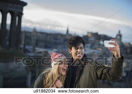 Picture - A young couple photograph themselves on Calton Hill with the background of the city of Edinburgh, capital of Scotland. Fotosearch