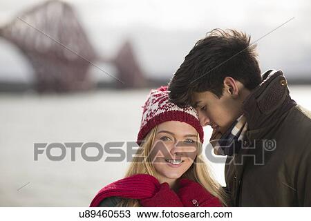 Stock Image - A young couple pose in front of the Forth Rail Bridge in Queensferry, near Edinburgh, Scotland. Fotosearch