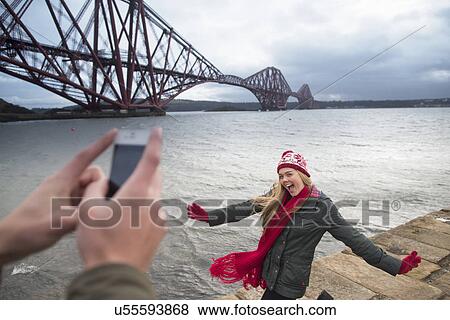Stock Photo - A young couple pose in front of the Forth Rail Bridge in Queensferry, near Edinburgh, Scotland. Fotosearch