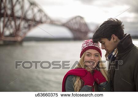 Stock Photography - A young couple pose in front of the Forth Rail Bridge in Queensferry, near Edinburgh, Scotland. Fotosearch