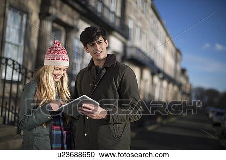 Stock Image - A young couple walk on Regent Terrace in Edinburgh Scotland and look at their tablet computer. Fotosearch