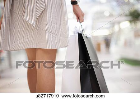 Stock Image - Backview of young woman with shopping bag. Fotosearch