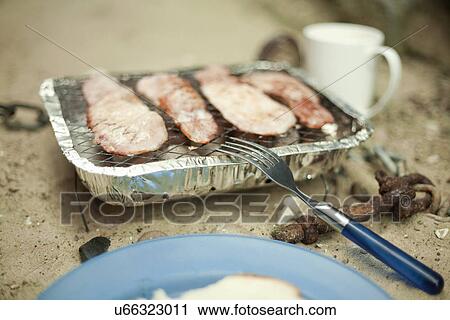 Stock Image - Bacon cooking on disposable barbeque. Fotosearch