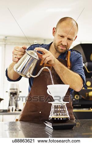 Stock Image - Barista pouring boiling water into coffee filter. Fotosearch
