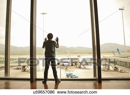 Stock Photograph - Boy looking out of window at airport. Fotosearch
