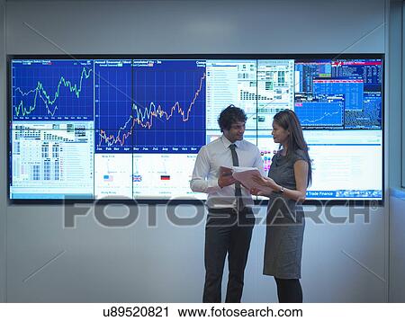 Stock Image - Business people meeting in front of graphical screens. Fotosearch