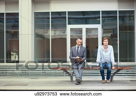 Businessman and young man sitting on train station bench View Large Photo Image Stock Image - Businessman and young man sitting on train station bench. Fotosearch