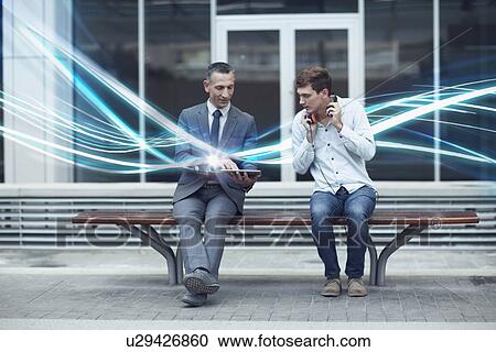 Stock Image - Businessman and young man watching digital tablet and waves of illumination. Fotosearch