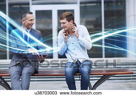 Stock Image - Businessman and young man watching digital tablet and waves of blue light. Fotosearch