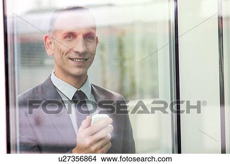 Picture - Businessman behind reflective glass holding smartphone. Fotosearch