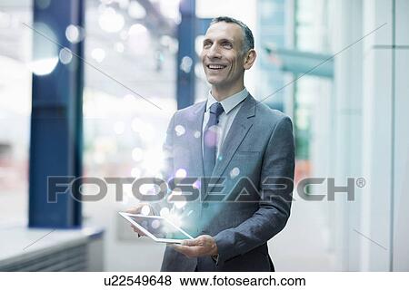 Businessman holding digital tablet with glowing lights coming out of it View Large Photo Image Stock Photo - Businessman holding digital tablet with glowing lights coming out of it. Fotosearch