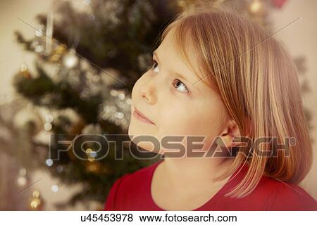 Stock Photo - Close up of girl, Christmas tree in background. Fotosearch